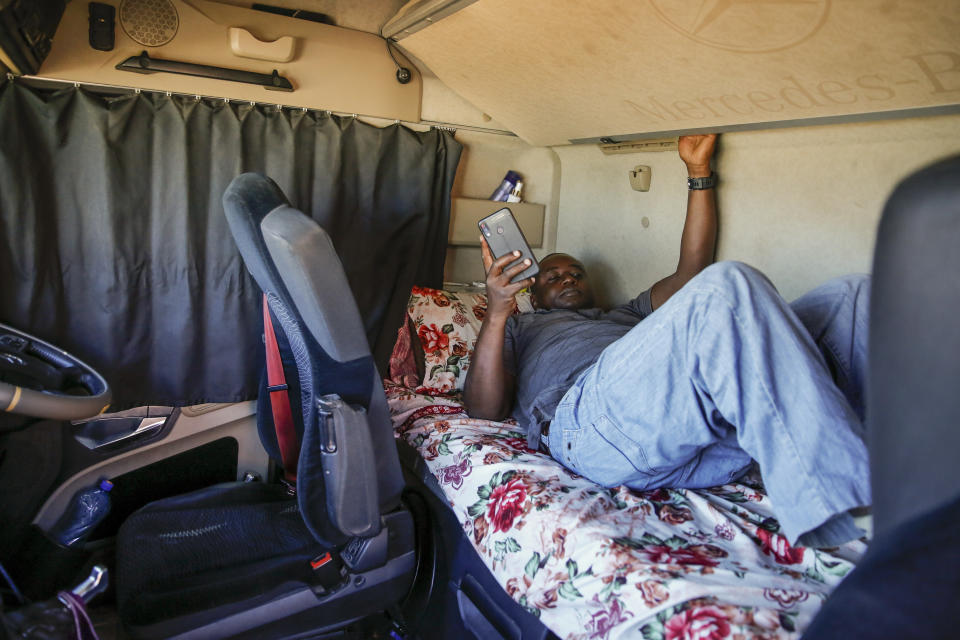 In this photo taken Monday, June 1, 2020, Kenyan truck driver Abdulkarim Rajab lies down in the cabin of his truck as he waits for his papers to be cleared and verified so that he can enter Kenya, on the Kenya side of the Namanga border crossing with Tanzania. Africa's long-haul truckers carry food, fuel and other essential supplies along dangerous roads, but now they say they are increasingly accused of carrying the coronavirus as well. “When I entered Tanzania, in every town that I would drive through, they would call me, ’You, corona, get away from here with your corona!’” said Rajab. (AP Photo/Brian Inganga)
