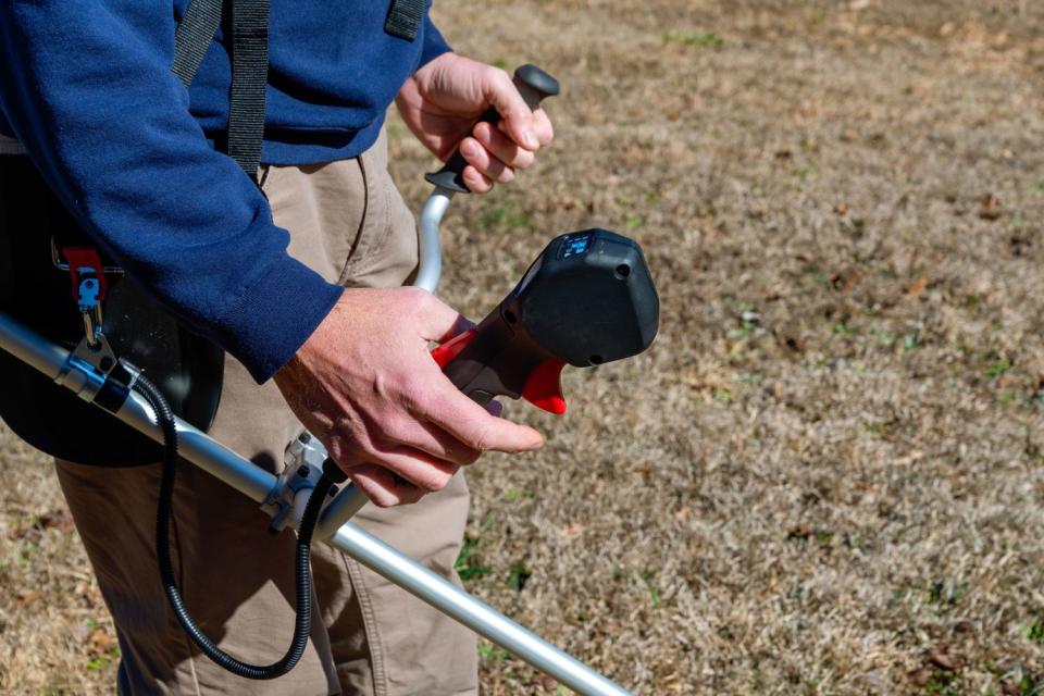 A person with their hand on the controls of the Makita cordless brush cutter during testing.