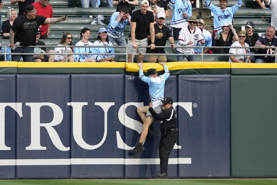 A baseball fan is pulled down by a security guard as he tries to climb the left center wall after running on the field at the start of a baseball game between the Chicago White Sox and the Tampa Bay Rays, Saturday, April 27, 2024, in Chicago. (AP Photo/Charles Rex Arbogast)