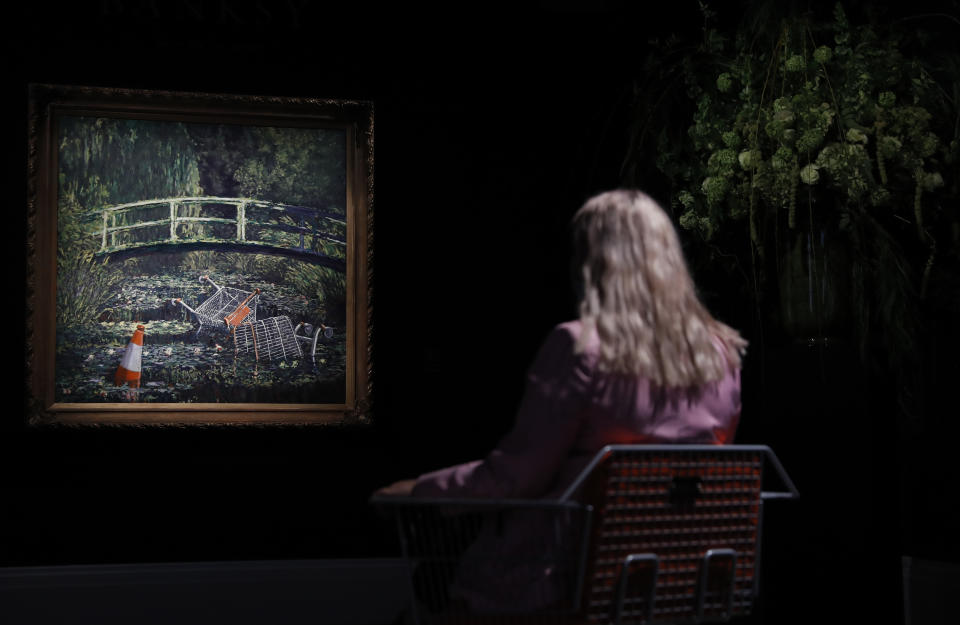 A member of staff poses in front of a work of art by Banksy entitled 'Show Me The Monet" at Sotheby's auction house in London, Friday, Oct. 16, 2020. The painting is valued at 3-5 million pounds (US$ 3.8-6.4 million ) when sold at auction on Oct. 21. (AP Photo/Alastair Grant)