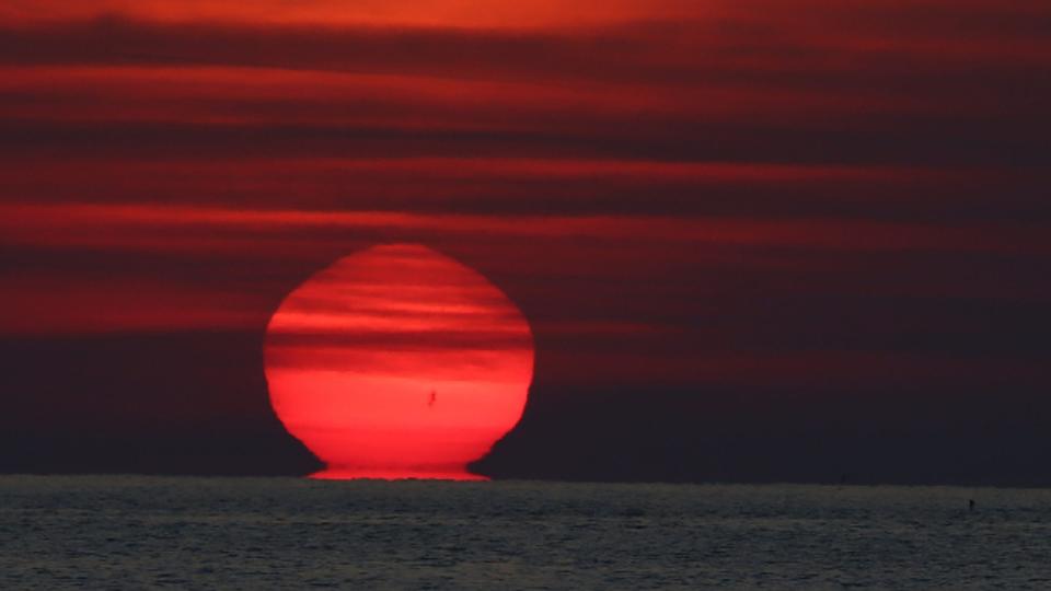 A red sun rises but appears to melt back towards the horizon