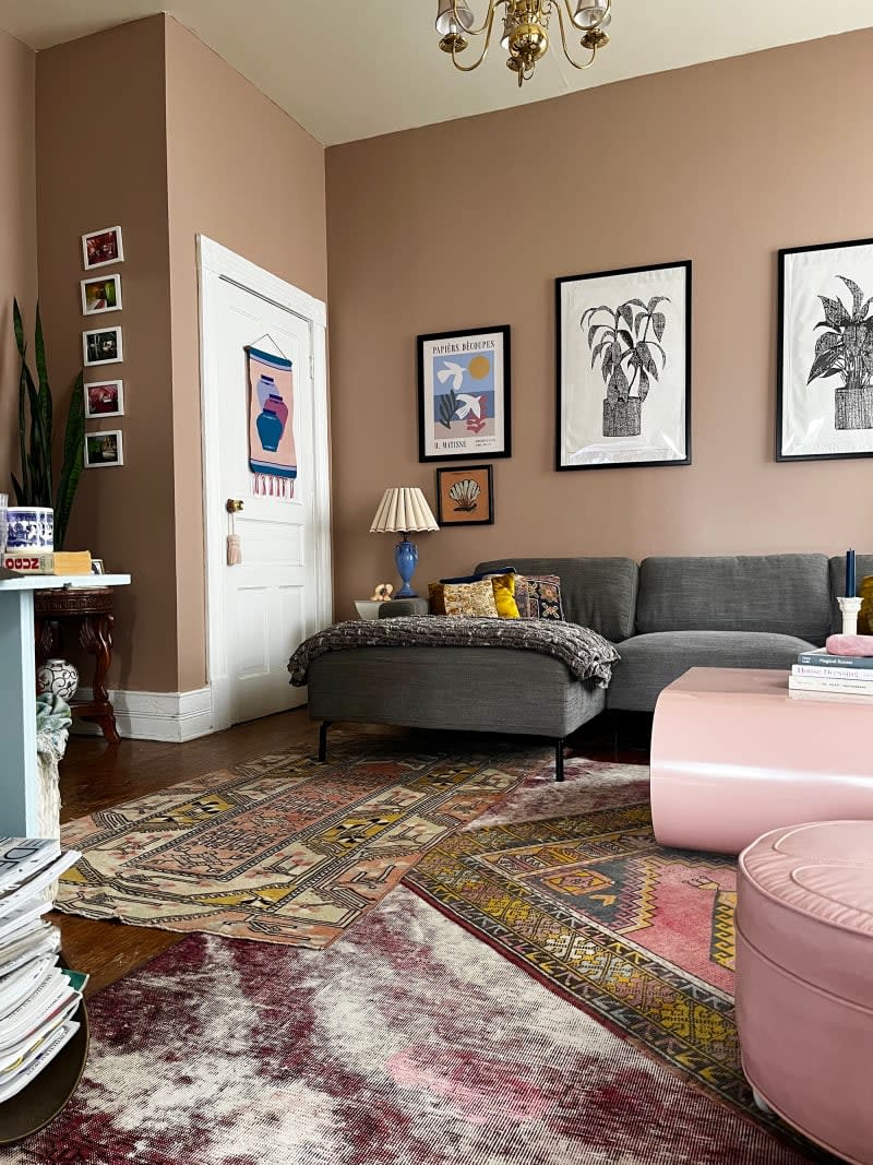 Gray sofa sits atop multiple area rugs in living room featuring art hung on pink brown walls.