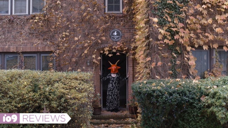 A woman in a red goat mask stands in a doorway