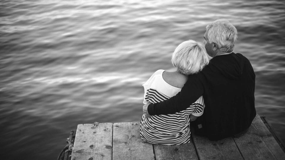 retired couple sitting on the edge of a dock by a lake