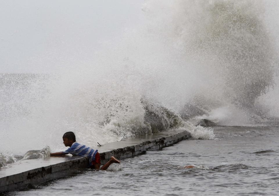 A boy holds on to the concrete bank as rough waves crash along the coast of Manila Bay brought by Super Typhoon Usagi in Navotas City, metro Manila September 21, 2013. The year's most powerful typhoon slammed into the Philippines' northernmost islands on Saturday, cutting communication and power lines, triggering landslides and inundating rice fields, officials said. Packing winds of 185 kph (114 mph) near the center and gusts of up to 220 kph, Typhoon Usagi weakened after hitting the Batanes island group, and is moving slowly west-northwest at 19 kph towards southern China, the weather bureau said. REUTERS/Romeo Ranoco (PHILIPPINES - Tags: DISASTER SOCIETY ENVIRONMENT TPX IMAGES OF THE DAY)