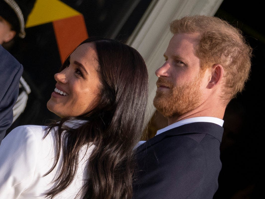 A close-up photo of Prince Harry (right) in a navy suit and Meghan Markle (left) in a white suit at the Invictus Games reception in The Hague, Netherlands.