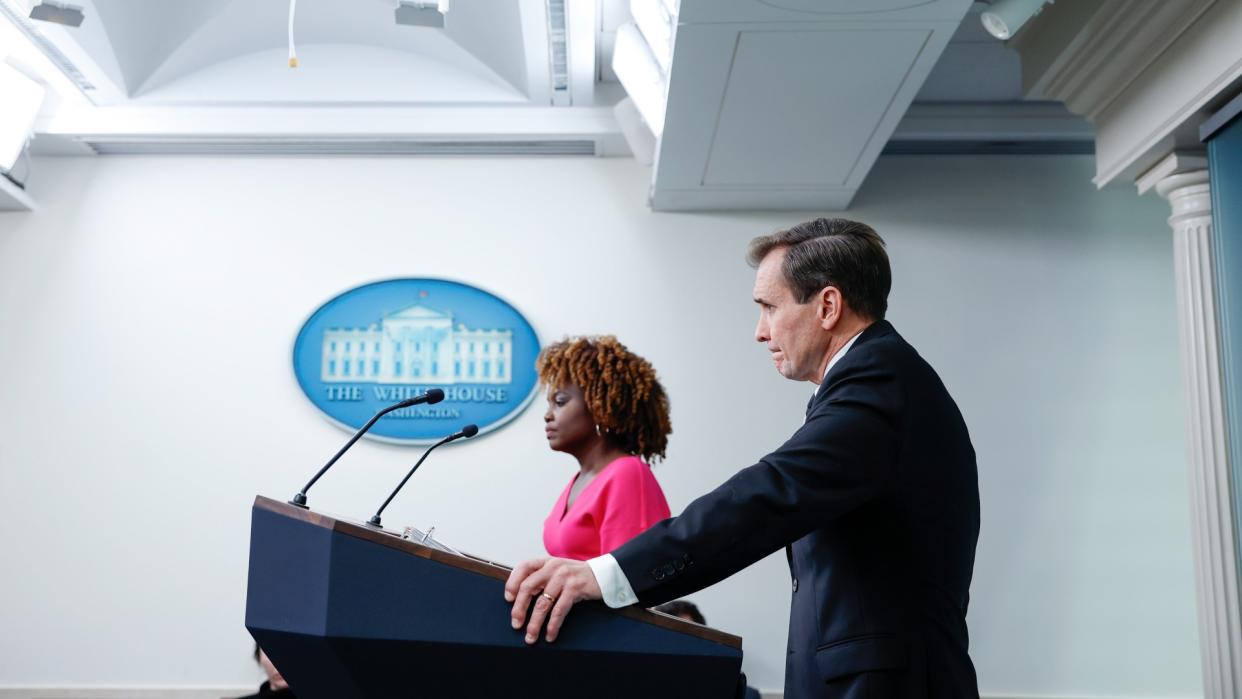  A person in a suit stands at a lectern under a sign reading "the white house". 