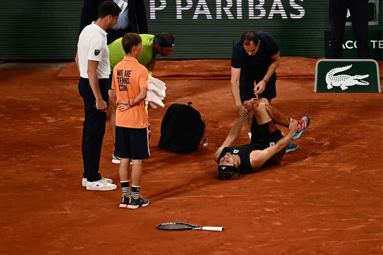 Alexander Zverev, tirado sobre el polvo de ladrillo de Roland Garros tras doblarse el tobillo; Rafael Nadal, su rival, lo observa