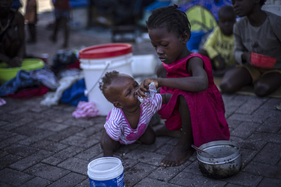 A girl helps a baby to drink water at the Hugo Chavez public square transformed into a refuge for families forced to leave their homes due to clashes between armed gangs, in Port-au-Prince, Haiti, Thursday, Oct. 20, 2022. (AP Photo/Ramon Espinosa)