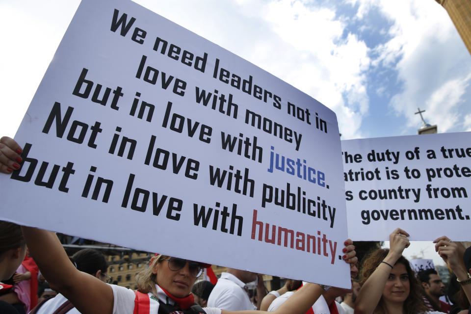 Anti-government protesters hold placards as they protest, in downtown Beirut, Lebanon, Sunday, Oct. 20, 2019. Tens of thousands of Lebanese protesters of all ages gathered Sunday in major cities and towns nationwide, with each hour bringing hundreds more people to the streets for the largest anti-government protests yet in four days of demonstrations. (AP Photo/Hussein Malla)