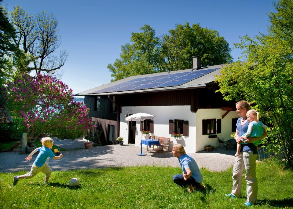 A photo of a young family in front of a home with solar panels on the roof.