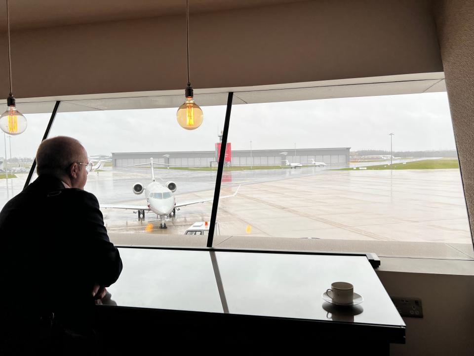 A man looks out the window at Farnborough Airport, with a Challenger 300 in the foreground.