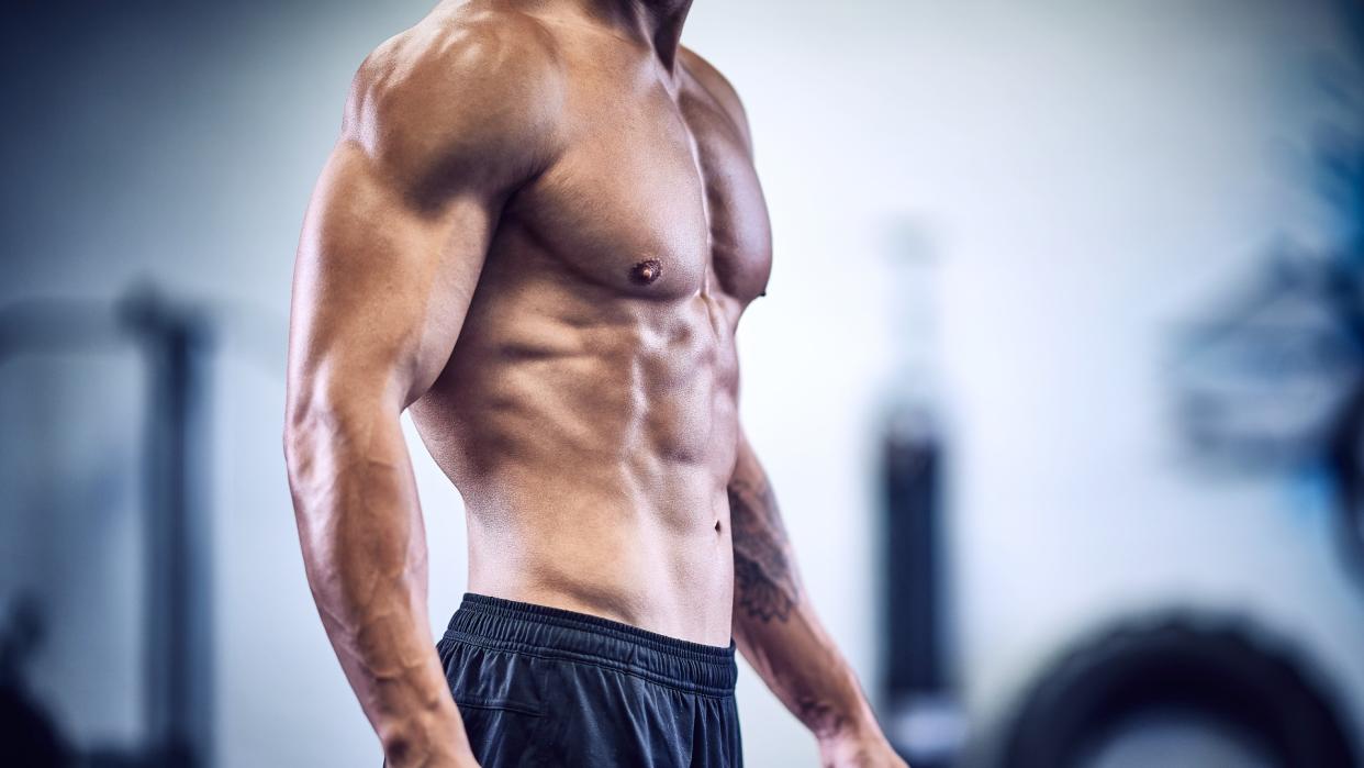  Man standing with top off showing muscled torso . 