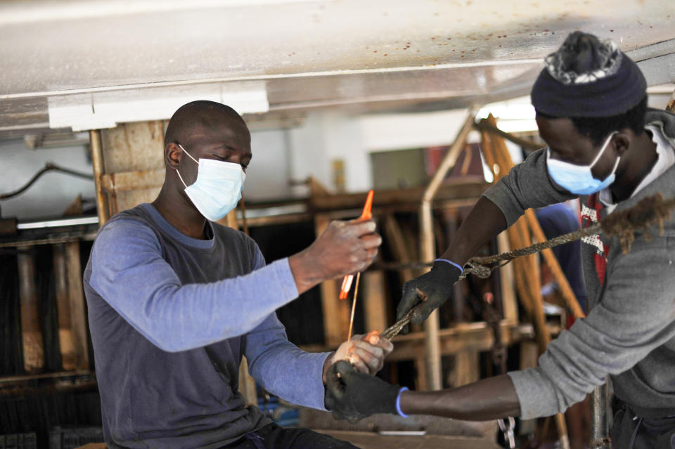 Waly Sarr, 30, right, and Ibrahima Mbaye, 41, both from Senegal, fix nets on the "Vincenzo Padre" fishing boat where they work as fishermen, in the Island of Lampedusa, southern Italy, Thursday, May 13, 2021. The tiny island of Lampedusa, which is closer to Africa than the Italian mainland, is in the throes of yet another season of migrant arrivals, and Mbaye and Sarr can only watch from shore as their fellow African countrymen risk their lives to get here via smugglers' boats. (AP Photo/Salvatore Cavalli)