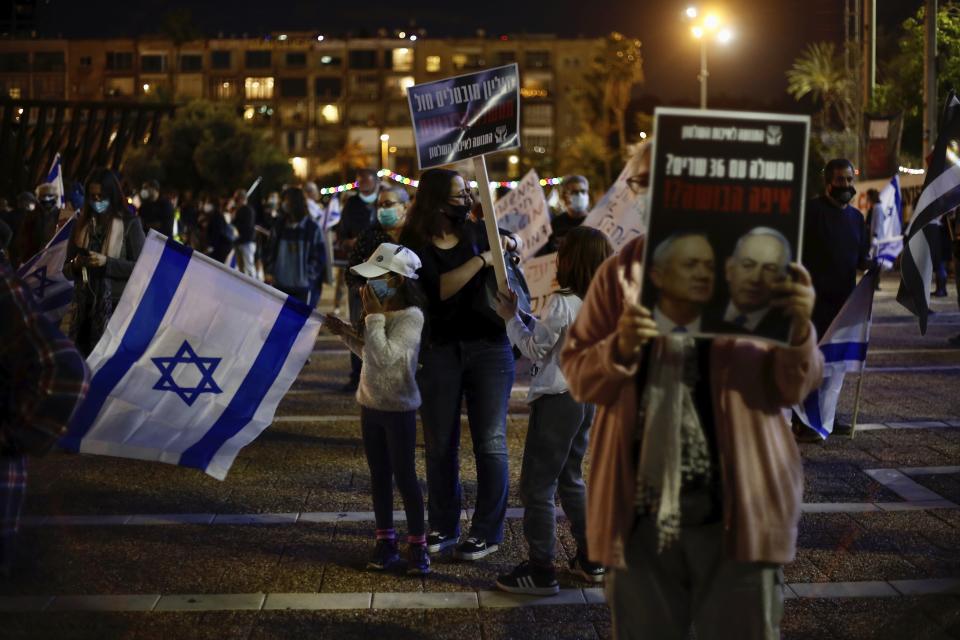 A woman holds a poster of Israeli Prime Minister Benjamin Netanyahu, right, and Benny Gantz ,left, that reads: 'a government with 36 ministers? Where is the shame?' during a protest against the government and the corruption, at Rabin square, in Tel Aviv, Israel, Saturday, May 2, 2020. Several thousand Israelis took to the streets on Saturday night, demonstrating against Prime Minister Benjamin Netanyahu's new coalition deal with his chief rival a day before the country's Supreme Court is to begin debating a series of legal challenges to the agreement.(AP Photo/Ariel Schalit)