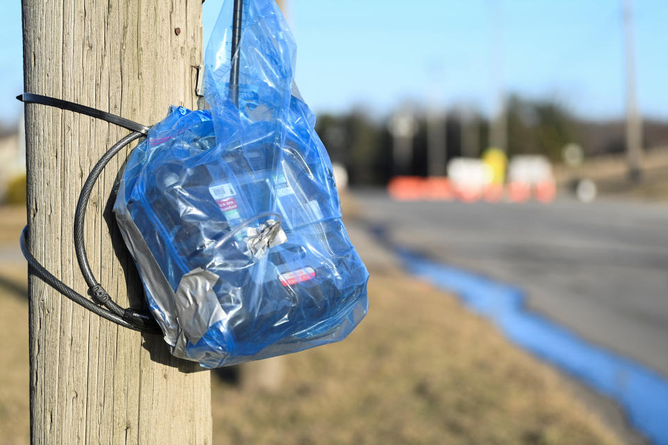 An air monitoring device wrapped in a blue plastic bag tied to a telephone pole, looking onto a stream, with some buildings in the far distance.