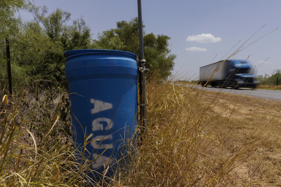 Una estación de agua para inmigrantes que contiene dentro bidones sellados de agua está ubicada al lado de una cerca próxima a una carretera en el condado rural Jim Hogg, en Texas, el martes 23 de julio de 2023. (AP Foto/Michael Gonzalez)