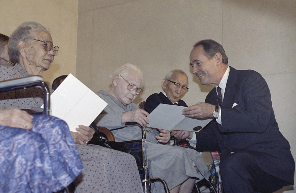 FILE - Attorney General Dick Thornburgh crouches to present $20,000 checks to three elderly Japanese Americans interned during World War II, during a ceremony at the Justice Department in Washington, Oct. 9, 1990. From left are Kisa Isari, Hau Dairiki and Mamoru Eto. They were also presented with a signed apology from President George H.W. Bush for their wrongful detention. Japanese Americans in their 70s and 80s inspired by the civil rights movement and who pushed for redress in the 1980s are among the most outspoken advocates of reparations for Black Americans. (AP Photo/Dennis Cook, File)