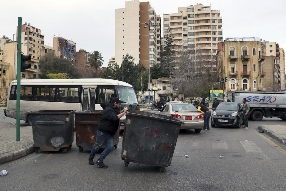 A man blocks a road with garbage containers during a general strike by public transport and labor unions paralyzed Lebanon to protest the country's deteriorating economic and financial conditions in Beirut, Lebanon, Thursday, Jan. 13, 2022. (AP Photo/Bilal Hussein)