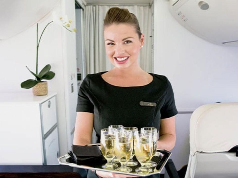 A cabin crew member posing with a tray of Champagne onboard the plane.