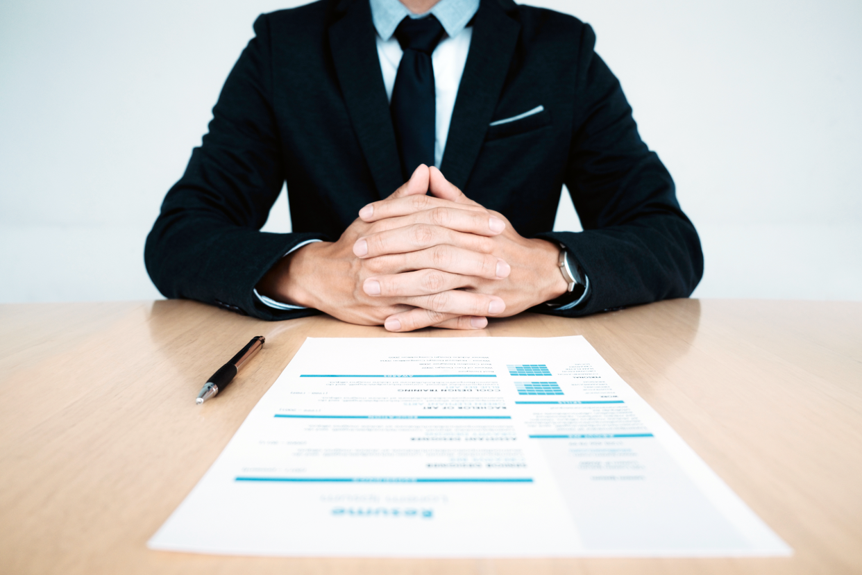 Boss sitting with hands folded at a desk with a resume in front of him