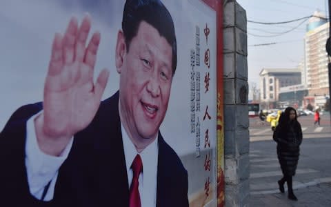 A woman walks past a poster of Chinese President Xi Jinping beside a street in Beijing  - Credit:  GREG BAKER/AFP