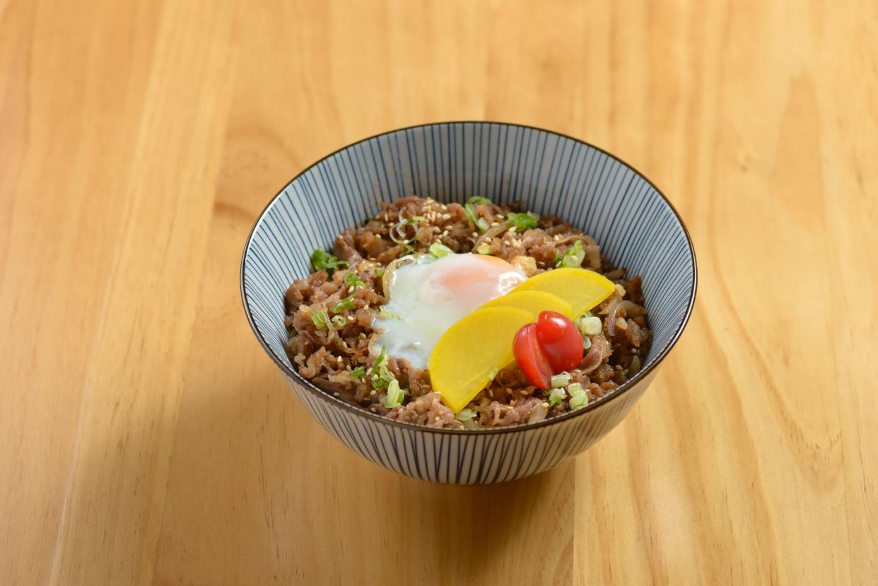 Tasty beef Gyudon with fried rice, egg and onion in a bowl on wooden background top view of japanese food