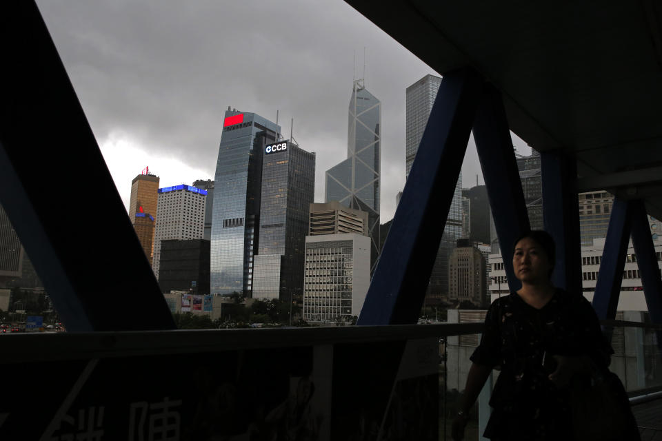 In this June 10, 2019, photo, a woman walks near the skyline of Hong Kong at Central, a business district of Hong Kong. It’s still the world’s “freest” economy, one of the biggest global financial centers and a scenic haven for tycoons and tourists, but the waves of protests rocking Hong Kong are exposing strains unlikely to dissipate as communist-ruled Beijing’s influence grows.(AP Photo/Kin Cheung)