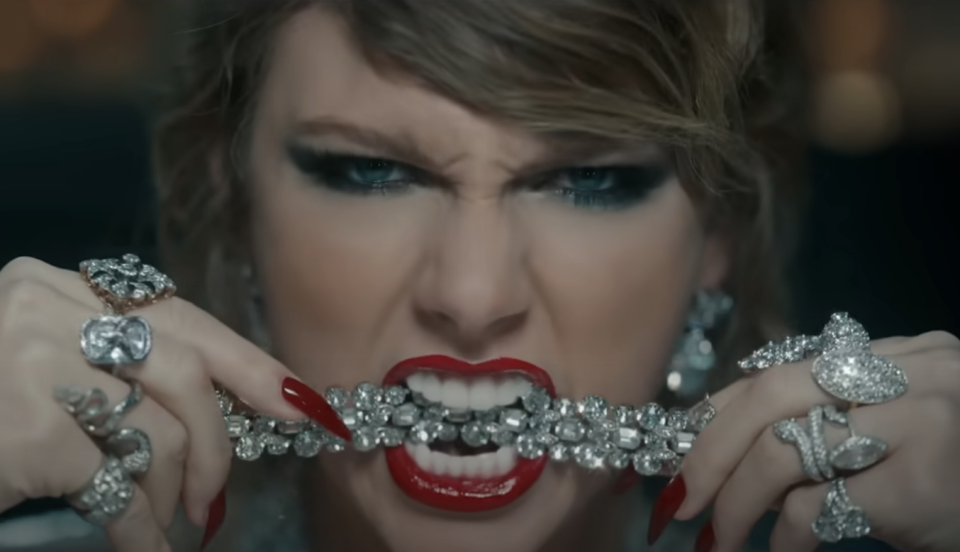 Taylor Swift biting a string of diamonds, with intense expression, adorned with glittering jewelry