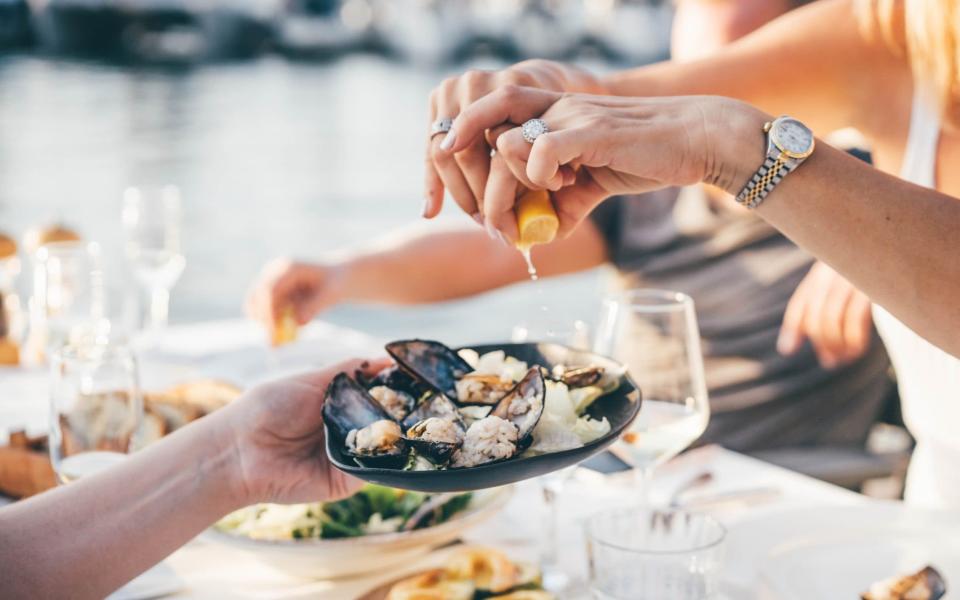 Close-up of a woman's hand squeezing lemon juice onto mussels surrounded by small plates