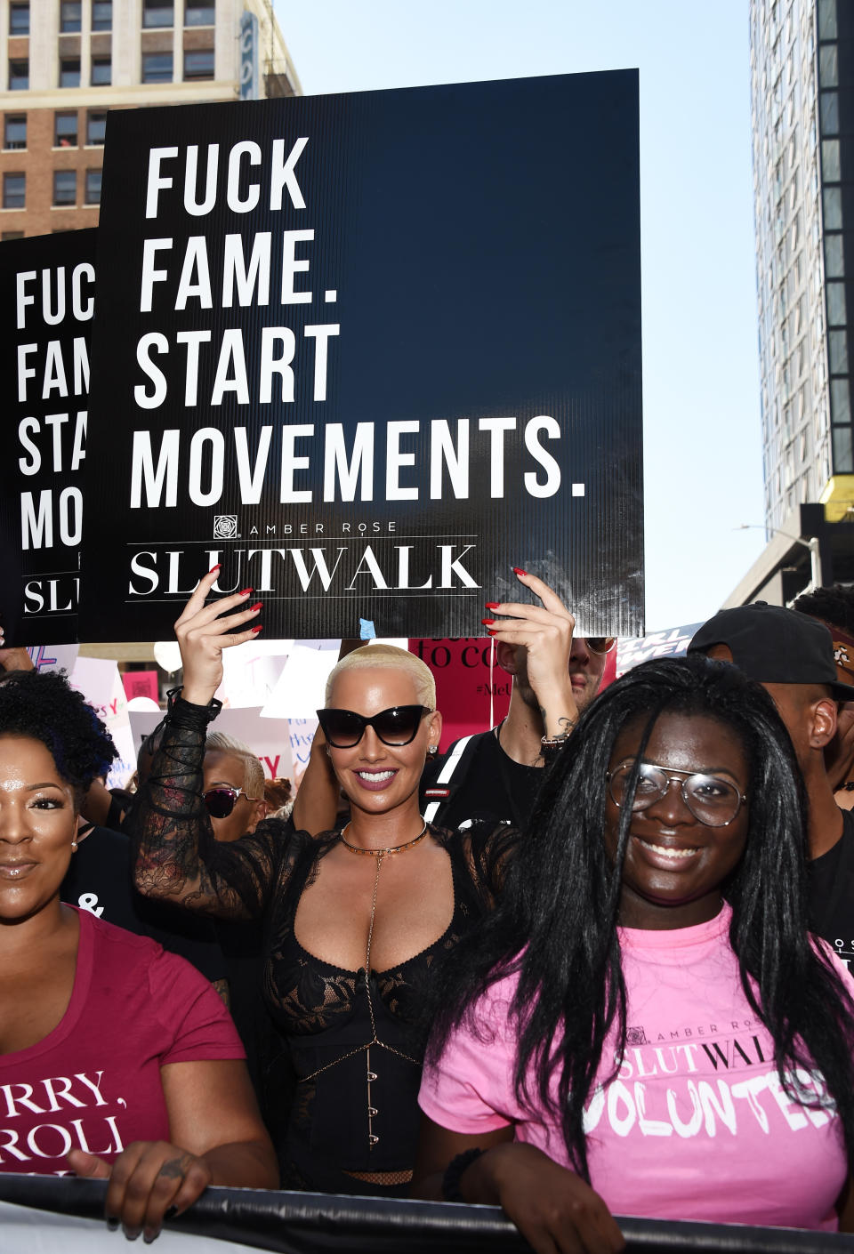 Amber Rose at SlutWalk holding a sign that reads, "F*ck Fame. Start Movements." She is surrounded by participants displaying supportive expressions