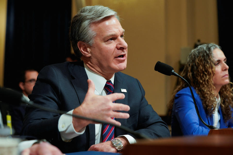 Christopher Wray, seated, speaks at a microphone.