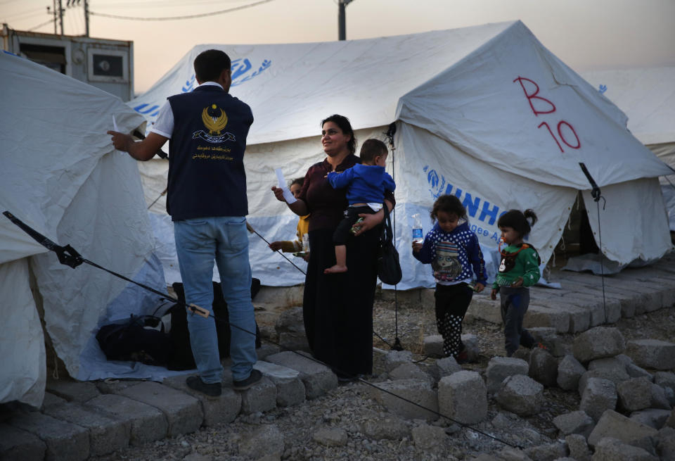 A Syrian woman with her children, who are newly displaced by the Turkish military operation in northeastern Syria, receives a tent from a Kurdish humanitarian worker upon her arrival at the Bardarash camp, north of Mosul, Iraq, Wednesday, Oct. 16, 2019. The camp used to host Iraqis displaced from Mosul during the fight against the Islamic State group and was closed two years ago. The U.N. says more around 160,000 Syrians have been displaced since the Turkish operation started last week, most of them internally in Syria. (AP Photo/Hussein Malla)