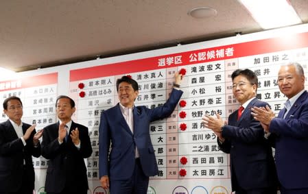 Japan's Prime Minister Shinzo Abe, who is also leader of the ruling Liberal Democratic Party (LDP), puts a rosette on the name of a candidate who is expected to win the upper house election, at the LDP headquarters in Tokyo