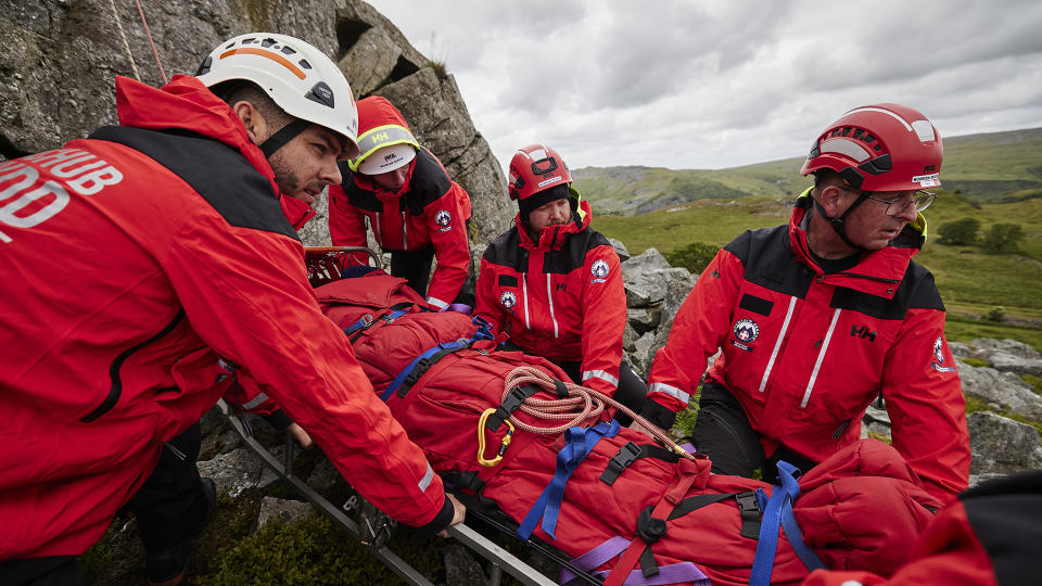 A group of mountain rescue volunteers guiding a stretcher down a mountainside.