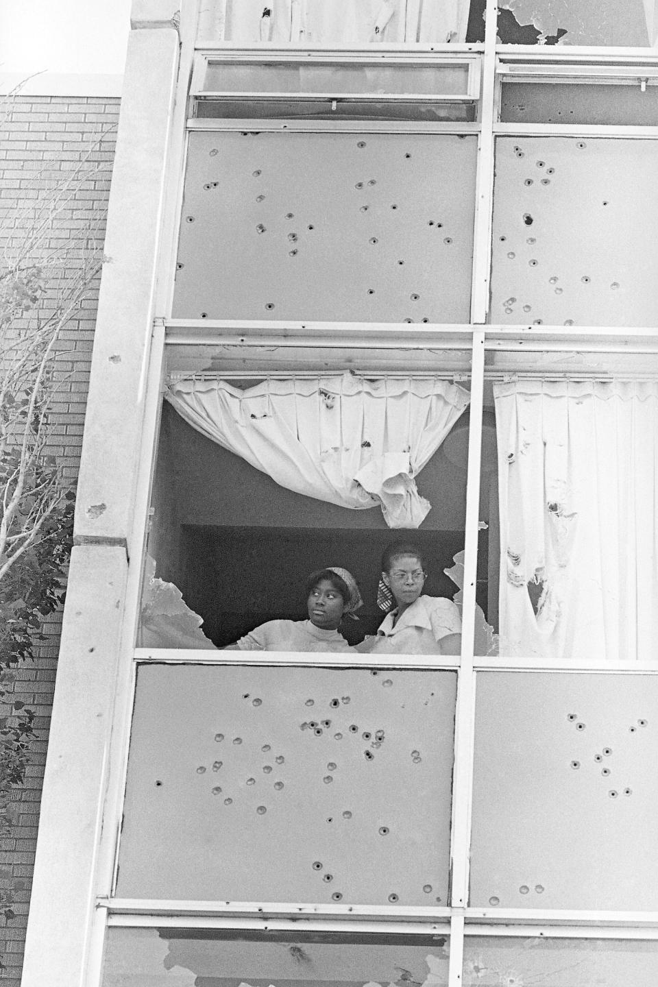 FILE - In this May 15, 1970, file photo, two students at Jackson State College, peer from a window at Alexander Hall, that was shot out by police on campus that morning, in Jackson, Miss. Two Black students died and 12 people were wounded as police shot indiscriminately, riddling the windows of the women's dormitory as officers claimed they had seen a sniper. The historically Black school canceled its 1970 commencement after the violent incident. Fifty-one years later, the school now called Jackson State University is honoring its Class of 1970, as members are being invited back to salute their academic achievements with a graduation ceremony Saturday, May 15, 2021. (AP Photo/Jack Thornell, File)