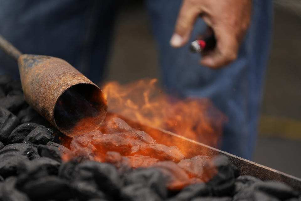 A member of The Shed BBQ and Blues Joint team lights the coals for the cooker as they compete at the World Championship Barbecue Cooking Contest, Friday, May 17, 2024, in Memphis, Tenn. (AP Photo/George Walker IV)