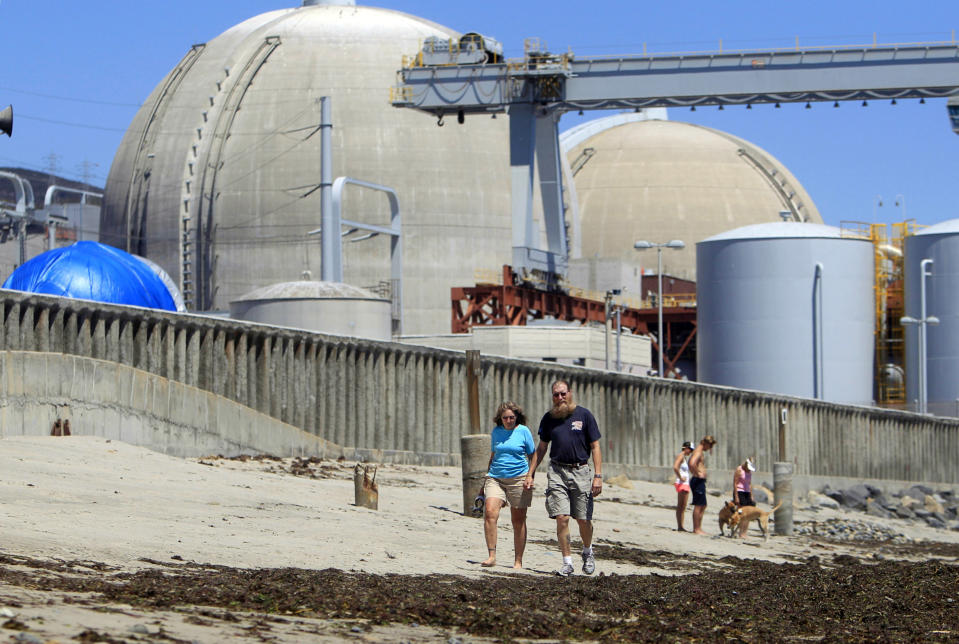 FILE - People walk on the sand near the shuttered San Onofre nuclear power plant in San Clemente, Calif., on June 30, 2011. The U.S. government has long struggled to find a permanent solution for storing or disposing of spent nuclear fuel generated by the nation's commercial nuclear power plants, and opposition in the Southwestern U.S. is flaring up again as New Mexico lawmakers debated a bill that would ban construction of such a facility without state consent. (AP Photo/Lenny Ignelzi, File)