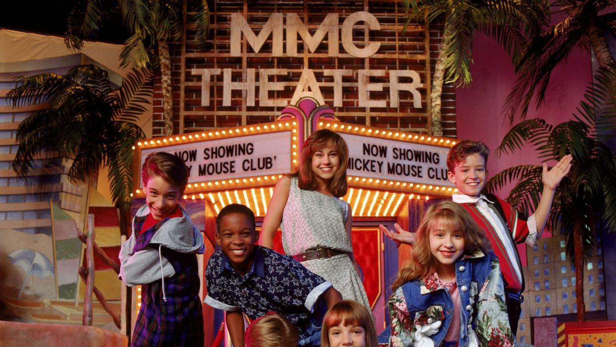 a group of kids stands and sits in front of a fake marque advertising the all new mickey mouse club