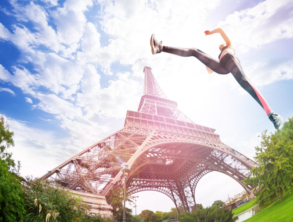 A woman in athletic clothing leaping in the air in front of the Eiffel Tower in Paris.