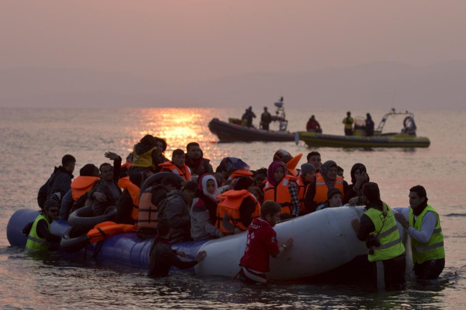 FILE - In this Sunday, March 20, 2016 file photo, volunteers help migrants and refugees on a dinghy as they arrive on the shore of the northeastern Greek island of Lesbos, after crossing the Aegean sea from Turkey. A Washington-based Syrian rights group filed on Thursday, Jan. 28, 2021 a case with the International Criminal Court calling for an investigation into alleged crimes against humanity by Greece for its treatment of refugees at its borders and in sprawling camps. (AP Photo/Petros Giannakouris, File)