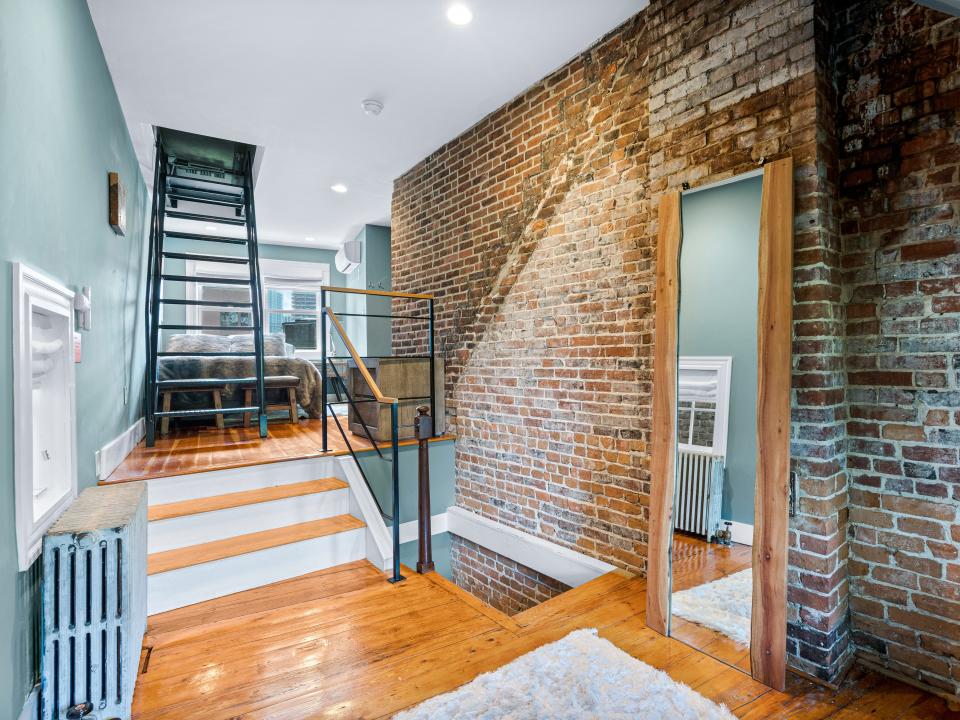 A room with blue walls on the left and exposed brick on the right. Two sets of stairs in the back left corner.