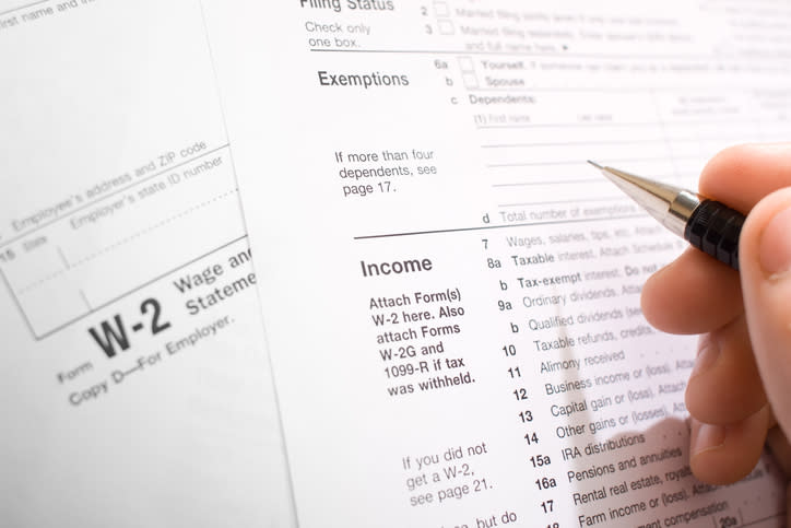 Close-up of a hand holding a pen and filling out a W-2 tax form, focusing on the Income section