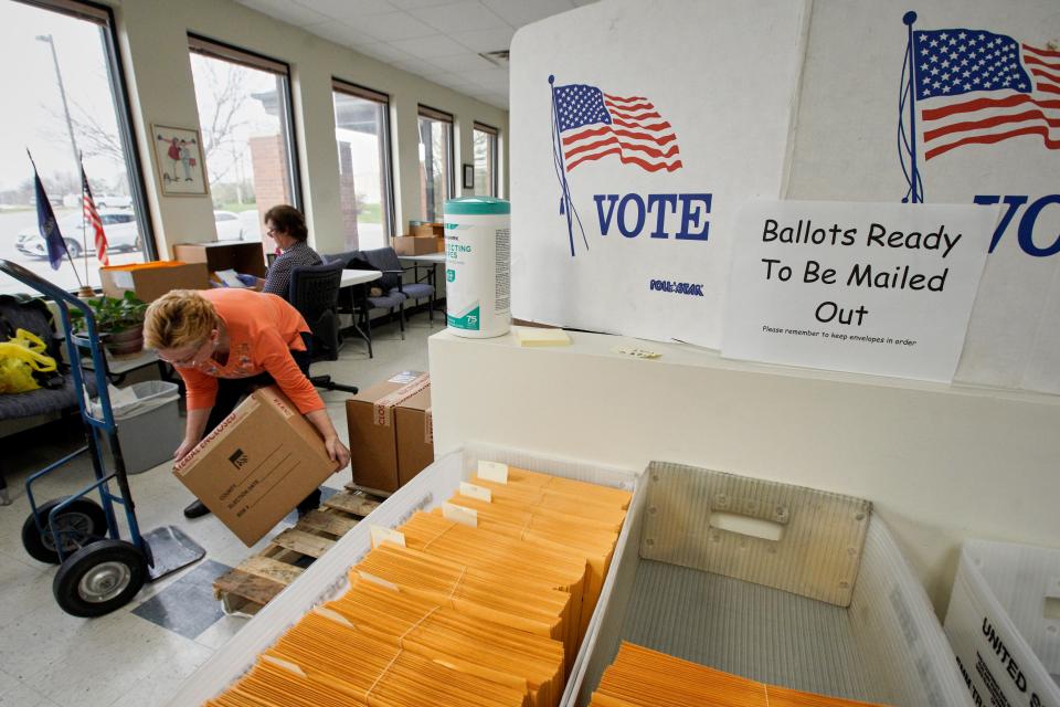 In this April 14, 2020 photo, Nadette Cheney picks up a box of printed ballots as others work on preparing mail-in ballots at the Lancaster County Election Committee offices in Lincoln, Neb. Officials in Nebraska are forging ahead with plans for the state’s May 12 primary despite calls from Democrats to only offer voting by mail and concerns from public health officials that in-person voting will help the coronavirus spread.  (AP Photo/Nati Harnik) ORG XMIT: NENH208