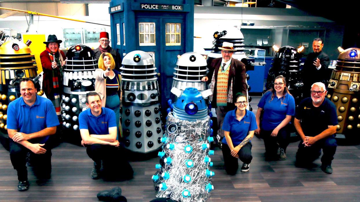 A group of employees kneeling down beside daleks and a blue telephone box prop 