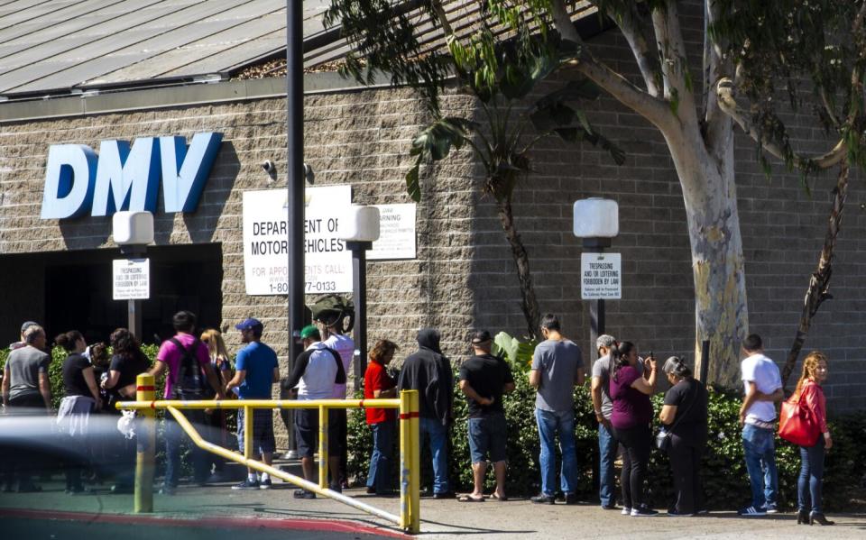 A line of people wait to be helped at a DMV office stretches around the building.