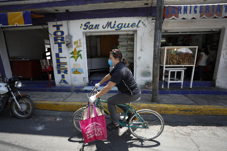 Angelica Aguilar De Alba, 47, rides her bike to deliver an order of five breakfast shakes, as she tries to keep the small Herbalife business she has owned for 10 years operating, in Santa Cruz Xochitepec in the Xochimilco district of Mexico City, Wednesday, April 1, 2020. Aguilar, who has closed her indoor seating and is now offering only take out or delivery options, estimates business has fallen 50% in the last two weeks due to measures to help contain the spread of the new coronavirus.  (AP Photo/Rebecca Blackwell)