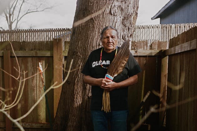 Indian Boarding School Survivor- Matthew Warbonnet poses with ceremonial feathers in his backyard. - Credit: Photographs by Annie Marie Musselman for Rolling Stone