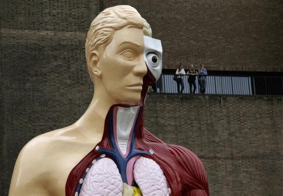 Visitors stand at a balcony behind the Damien Hirst sculpture "Hymn" outside the Tate Modern gallery in London August 21, 2012.