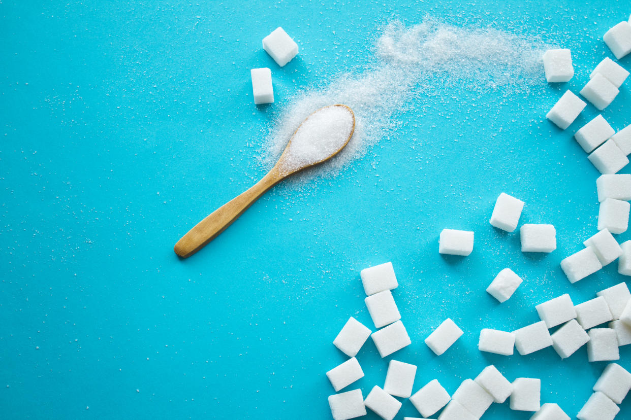 White sugar with spoon on blue background. Top view.